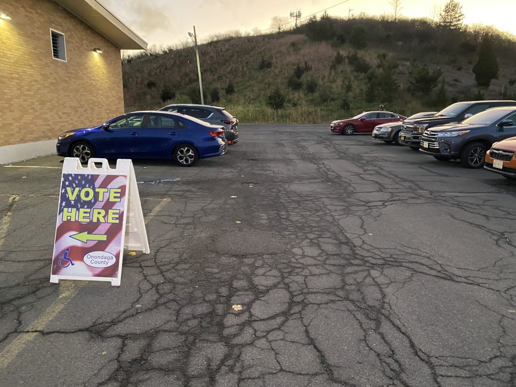 Cars parked and a sign pointing citizens in the direction to vote.