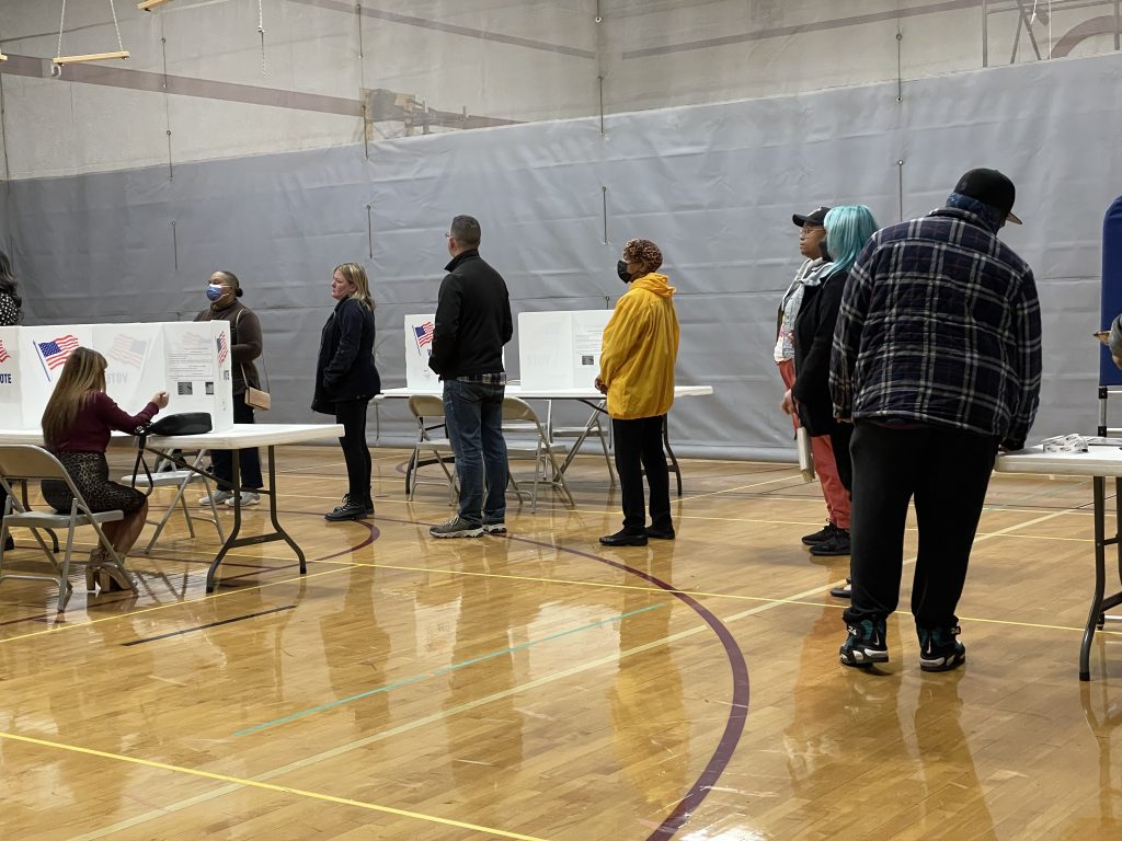 People are lined up in a row to vote in a gym.