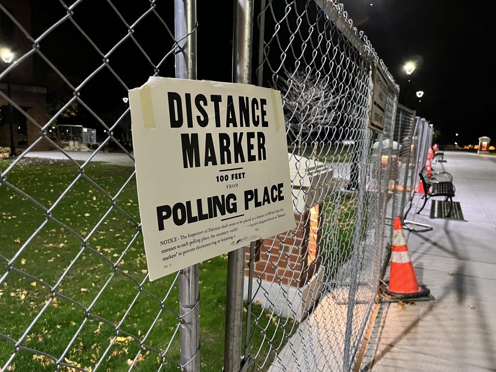 Polling place distance sign hung on construction fense.